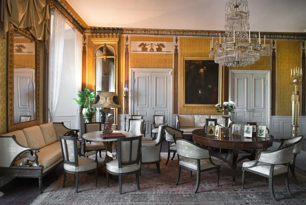 A room with silk furniture, round tables and a large chandelier on the ceiling.