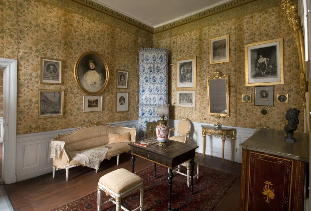 A room with silk furniture, a tiled stove and many paintings on the walls.