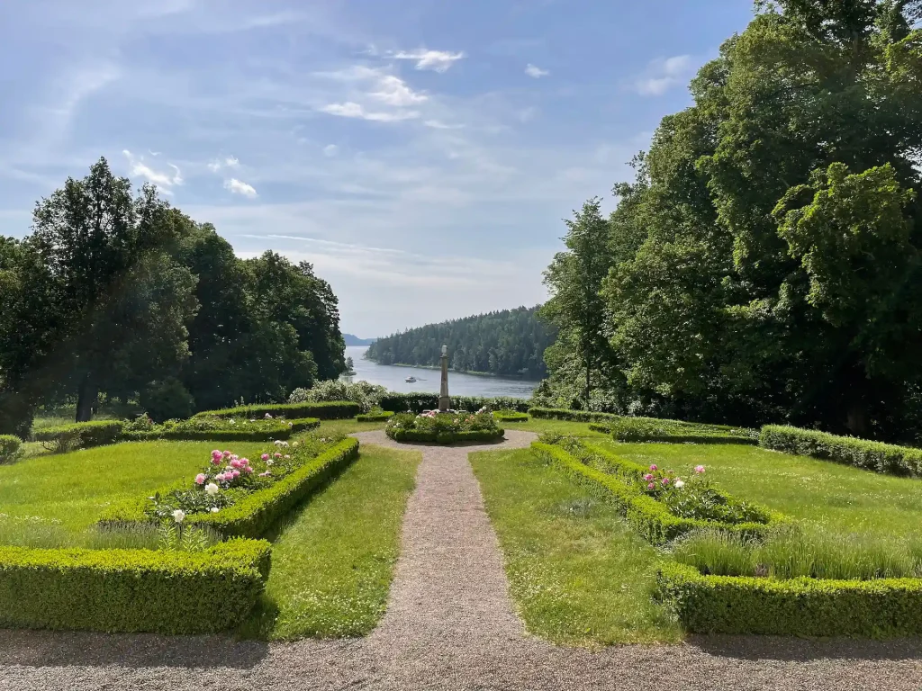 Siktlinje mot Kalvfjärden mellan låga buxbomshäckar, grusgångar och planteringar, en obelisk i fonden med vattnet bakom.