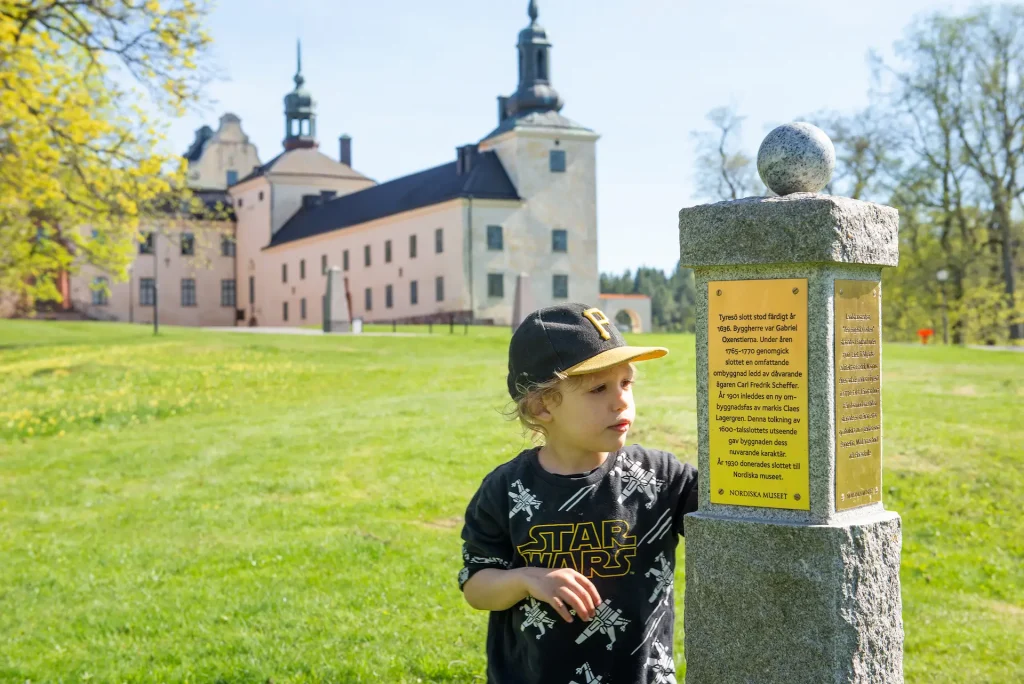 Ett barn tittar på en skylt på en granitpelare med ett slott i bakgrunden